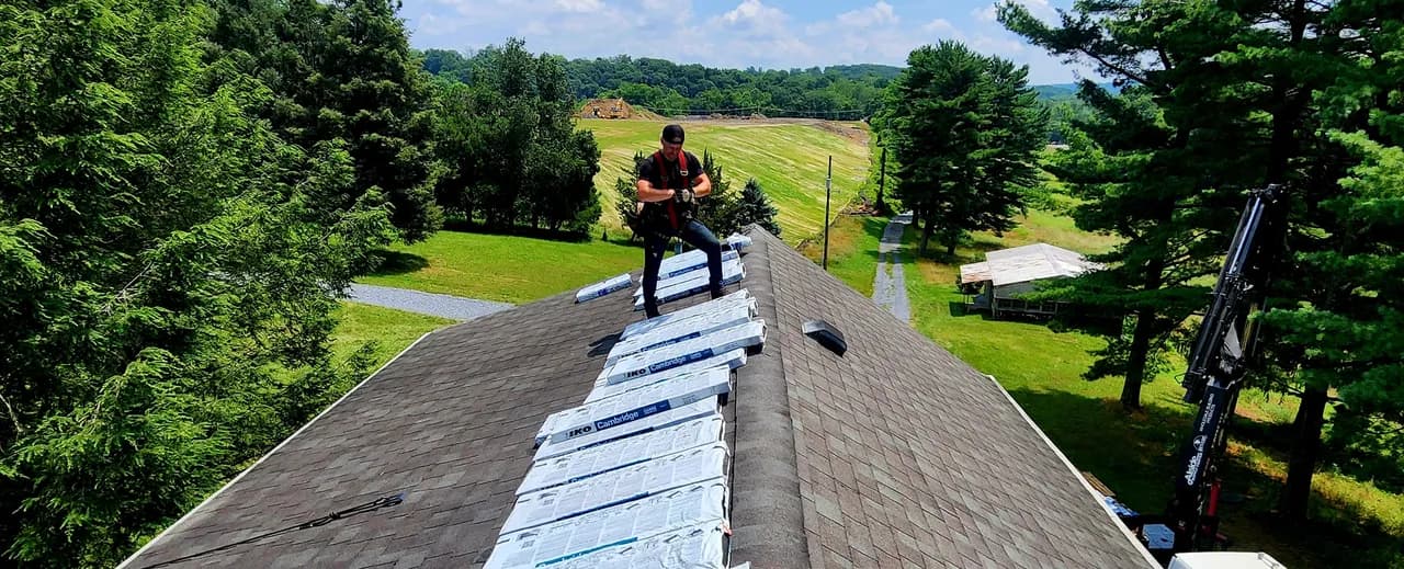 Roofer staging shingle bundles along the ridge of a Central PA home